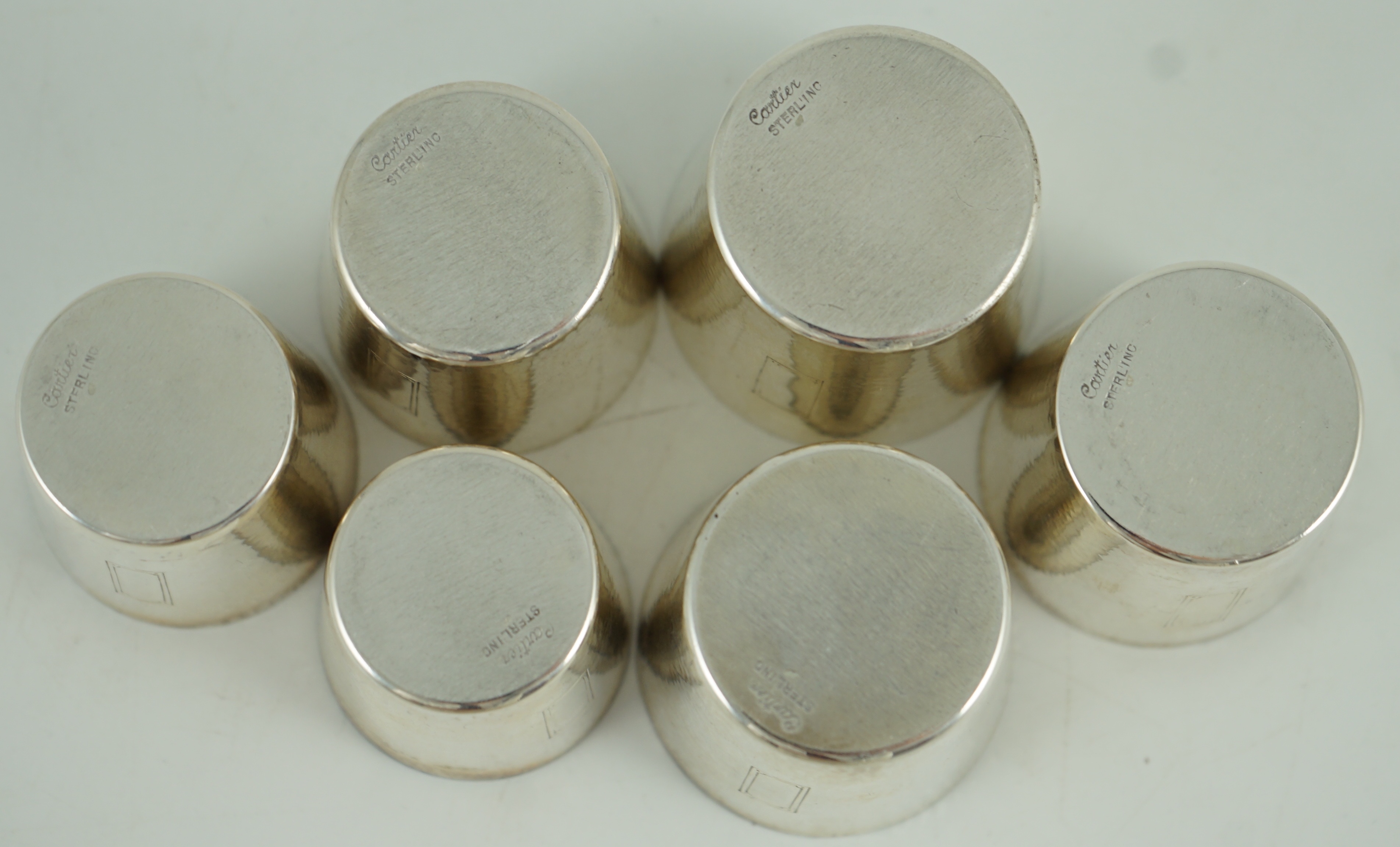 A 1930's/1940's planished sterling silver rectangular flask by Ahrendt & Kautzman, retailed by Cartier and six sterling similar graduated tots, signed Cartier